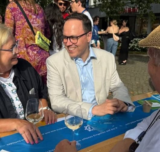 Dirk Panter sitzt mit anderen Menschen an einem Tisch im Freien